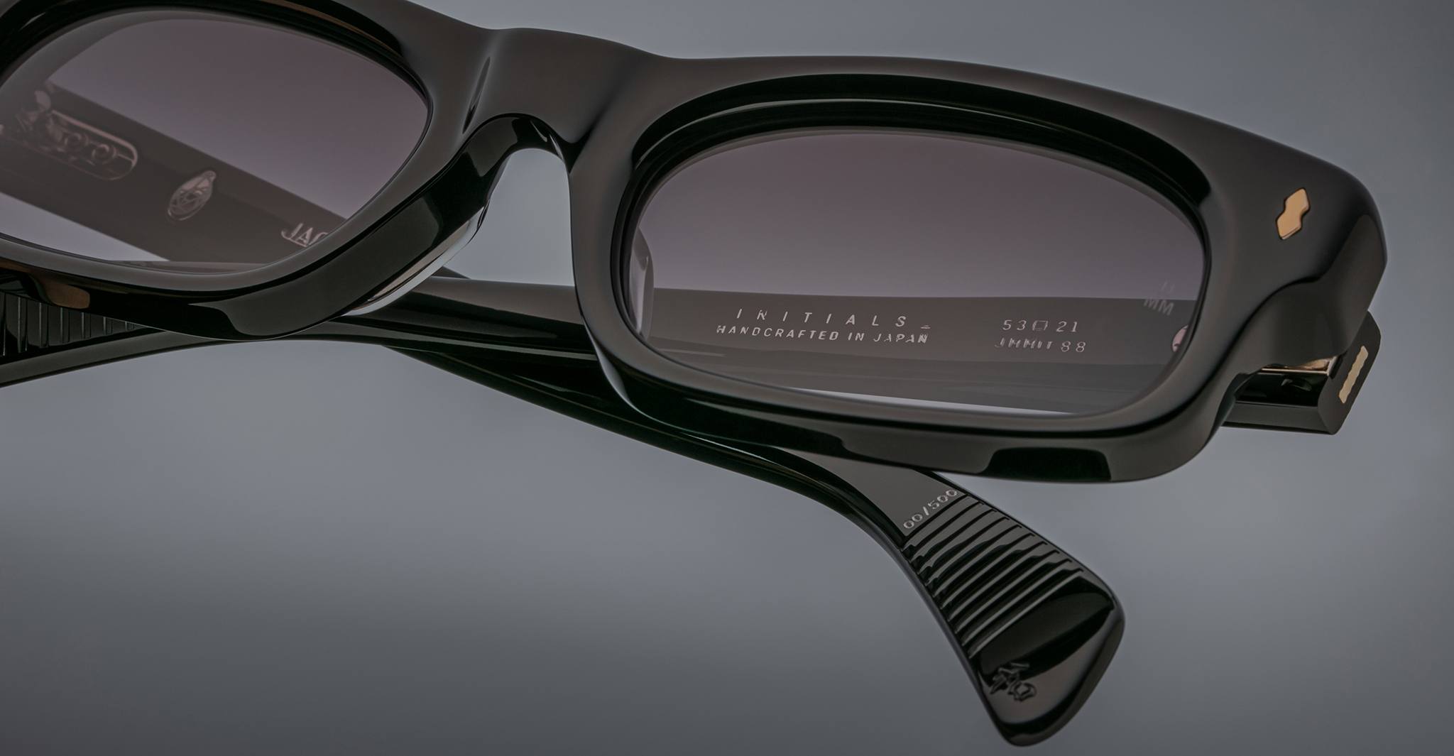 Close-up of Jacques Marie Mage Initials black micro-frame rectangular sunglasses with dark lenses, showing engraved "INITIALS HANDCRAFTED IN JAPAN" branding inside these limited-edition Jacques Marie Mage frames.