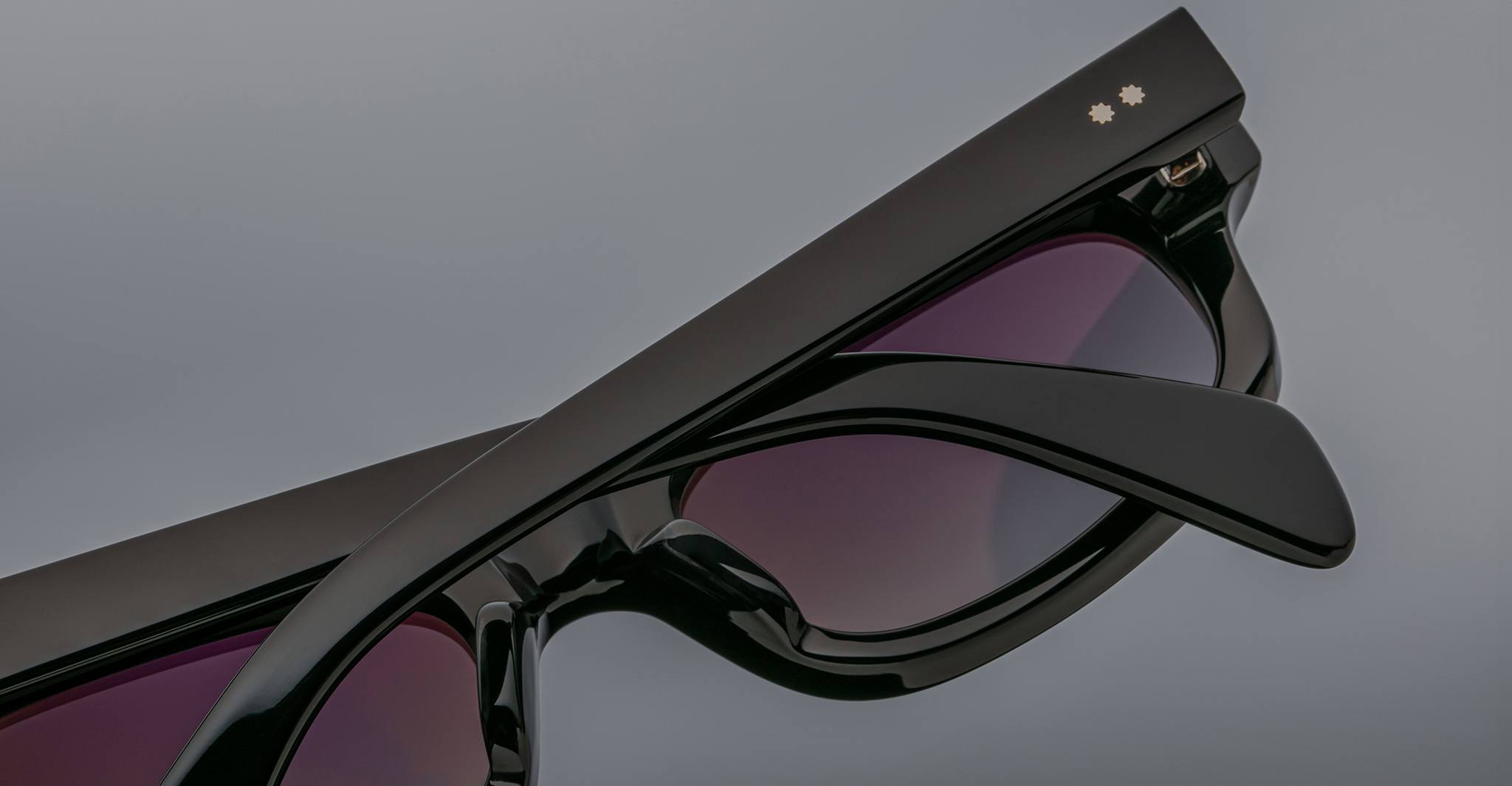 Close-up of Jacques Marie Mage Initials micro-frame sunglasses in black with purple-tinted lenses and two star-shaped details on the temple—a striking limited-edition design by Jacques Marie Mage.