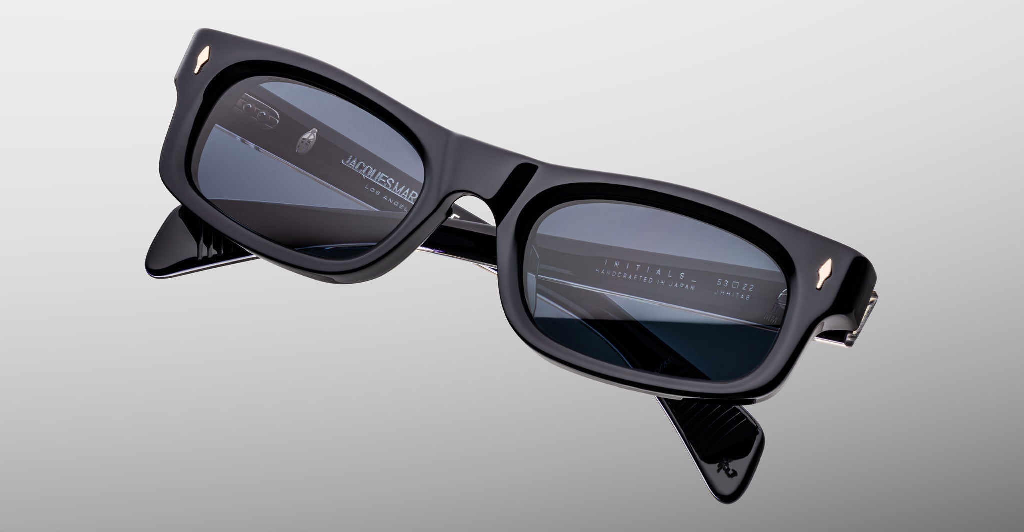The Jacques Marie Mage Initials by Jacques Marie Mage are black micro-frame smart glasses with rectangular lenses, displaying digital text and icons on the right lens against a plain light background.
