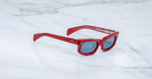 Jacques Marie Mage Initials sunglasses with red frames and dark lenses rest on a white marble surface, showcasing the brand's exclusive limited-edition style.