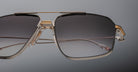 Close-up of Jacques Marie Mage Jagger oversized aviator sunglasses by Jacques Marie Mage, featuring black gradient lenses, a beta titanium bridge, and gold accents against a plain background.
