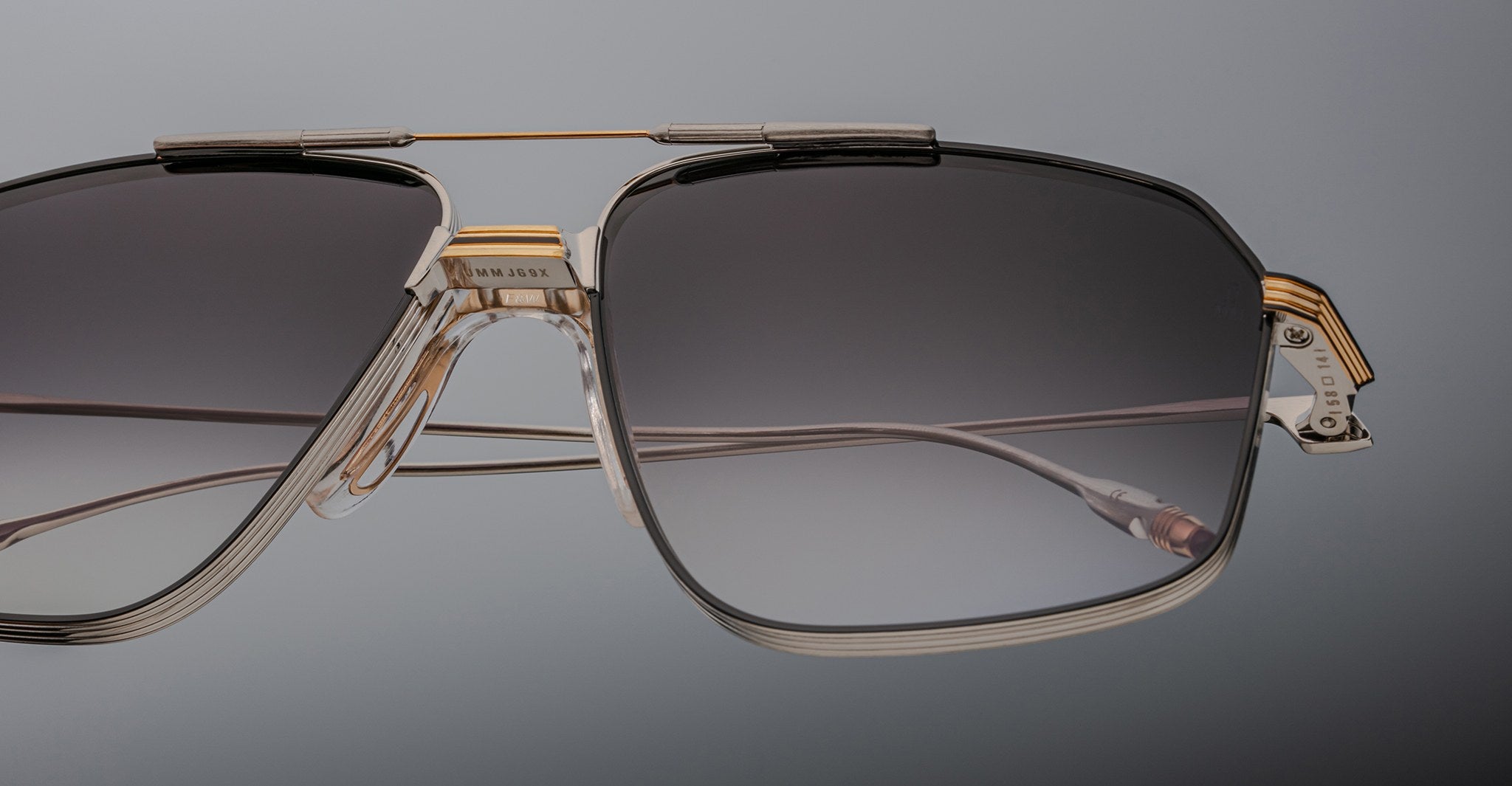 Close-up of Jacques Marie Mage Jagger oversized aviator sunglasses by Jacques Marie Mage, featuring black gradient lenses, a beta titanium bridge, and gold accents against a plain background.