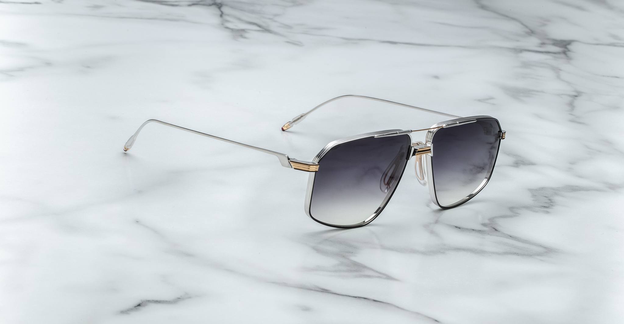 The Jacques Marie Mage Jagger sunglasses, featuring oversized aviator frames in silver beta titanium with gradient dark lenses, are displayed on a white marble surface.