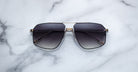 A pair of dark, oversized Jacques Marie Mage Jagger aviator sunglasses with thin beta titanium frames by Jacques Marie Mage, shown on a white marble surface.