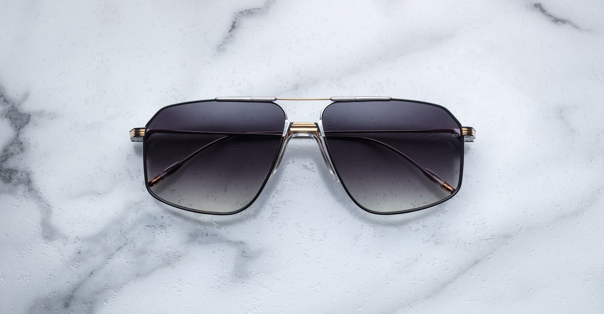 A pair of dark, oversized Jacques Marie Mage Jagger aviator sunglasses with thin beta titanium frames by Jacques Marie Mage, shown on a white marble surface.