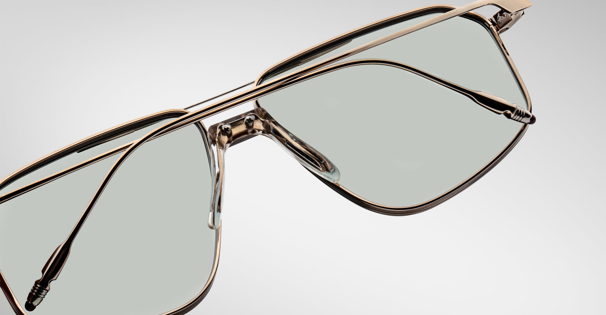 Close-up of Jacques Marie Mage Jagger oversized aviator sunglasses by Jacques Marie Mage, showcasing gold metal frames, beta titanium accents, clear nose pads, and light gray tinted lenses against a plain background.