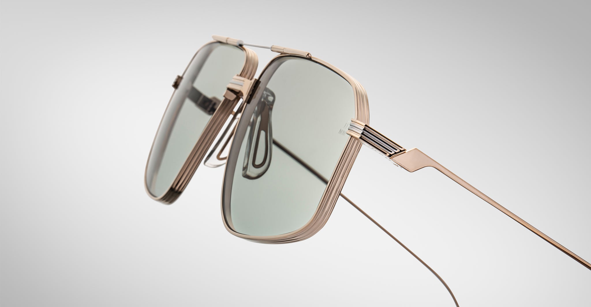 Close-up of Jacques Marie Mage Jagger sunglasses featuring gold beta titanium frames and rectangular green-tinted lenses by Jacques Marie Mage, displayed against a plain light gray background.