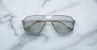 Jacques Marie Mage Jagger oversized aviator sunglasses by Jacques Marie Mage, featuring gold beta titanium frames and tinted lenses, are shown on a white marble surface.
