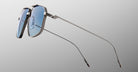 A pair of Jacques Marie Mage Jagger oversized aviator sunglasses, featuring silver frames and blue-tinted lenses, is displayed from a side angle on a light gray background.