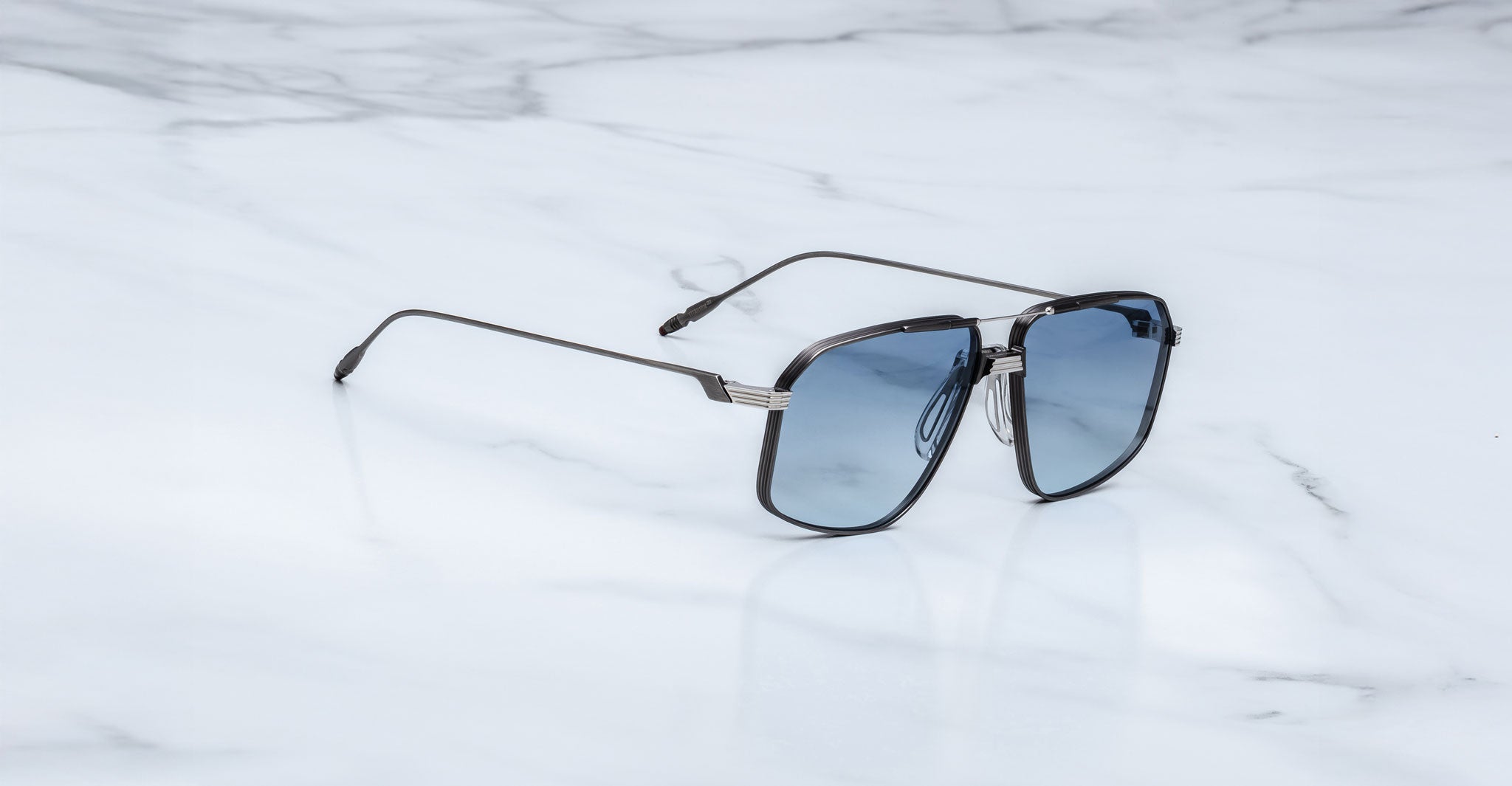 The Jacques Marie Mage Jagger oversized aviator sunglasses with blue tinted lenses from Jacques Marie Mage rest elegantly on a white marble surface.
