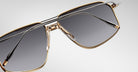 Close-up of Jacques Marie Mage Jagger sunglasses by Jacques Marie Mage, showcasing oversized aviator style with gold rims, dark tinted lenses, and sleek black temples against a light background.
