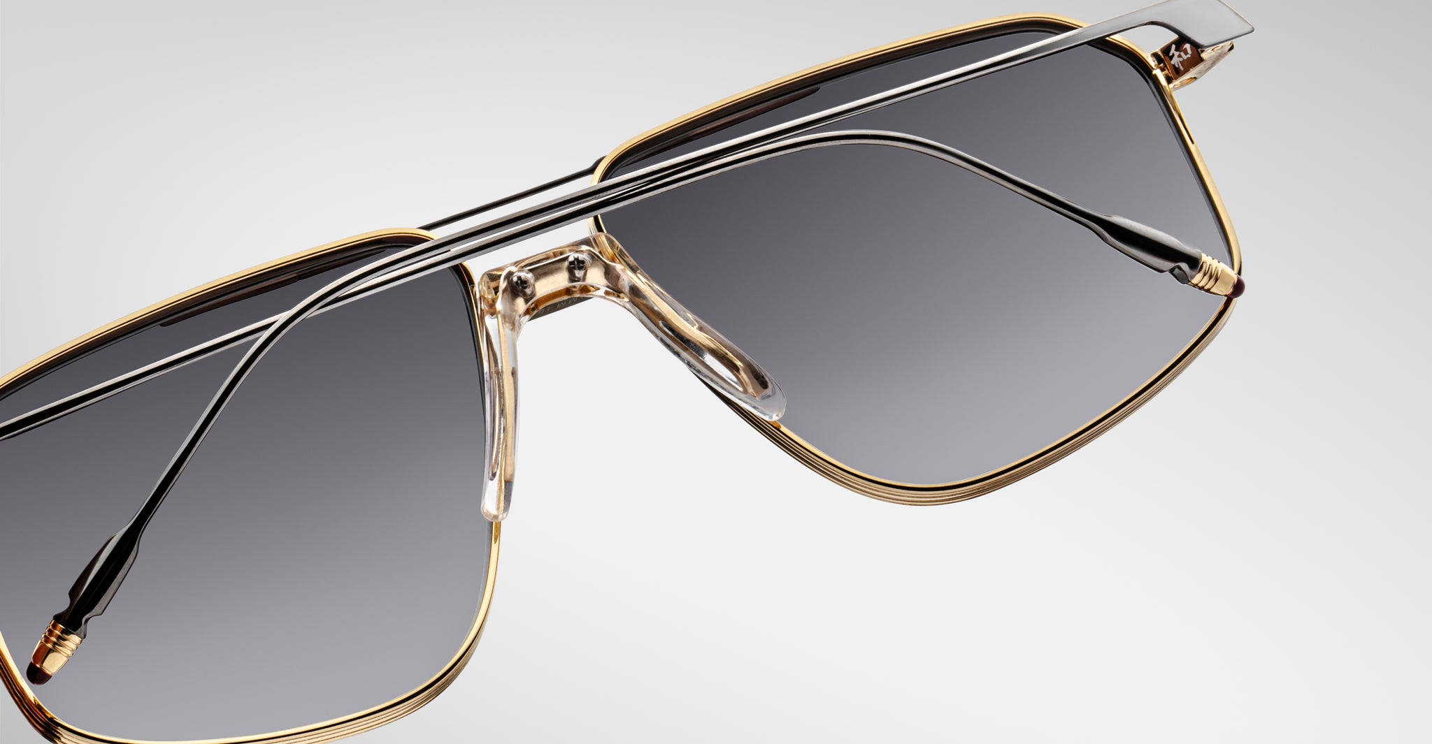 Close-up of Jacques Marie Mage Jagger sunglasses by Jacques Marie Mage, showcasing oversized aviator style with gold rims, dark tinted lenses, and sleek black temples against a light background.