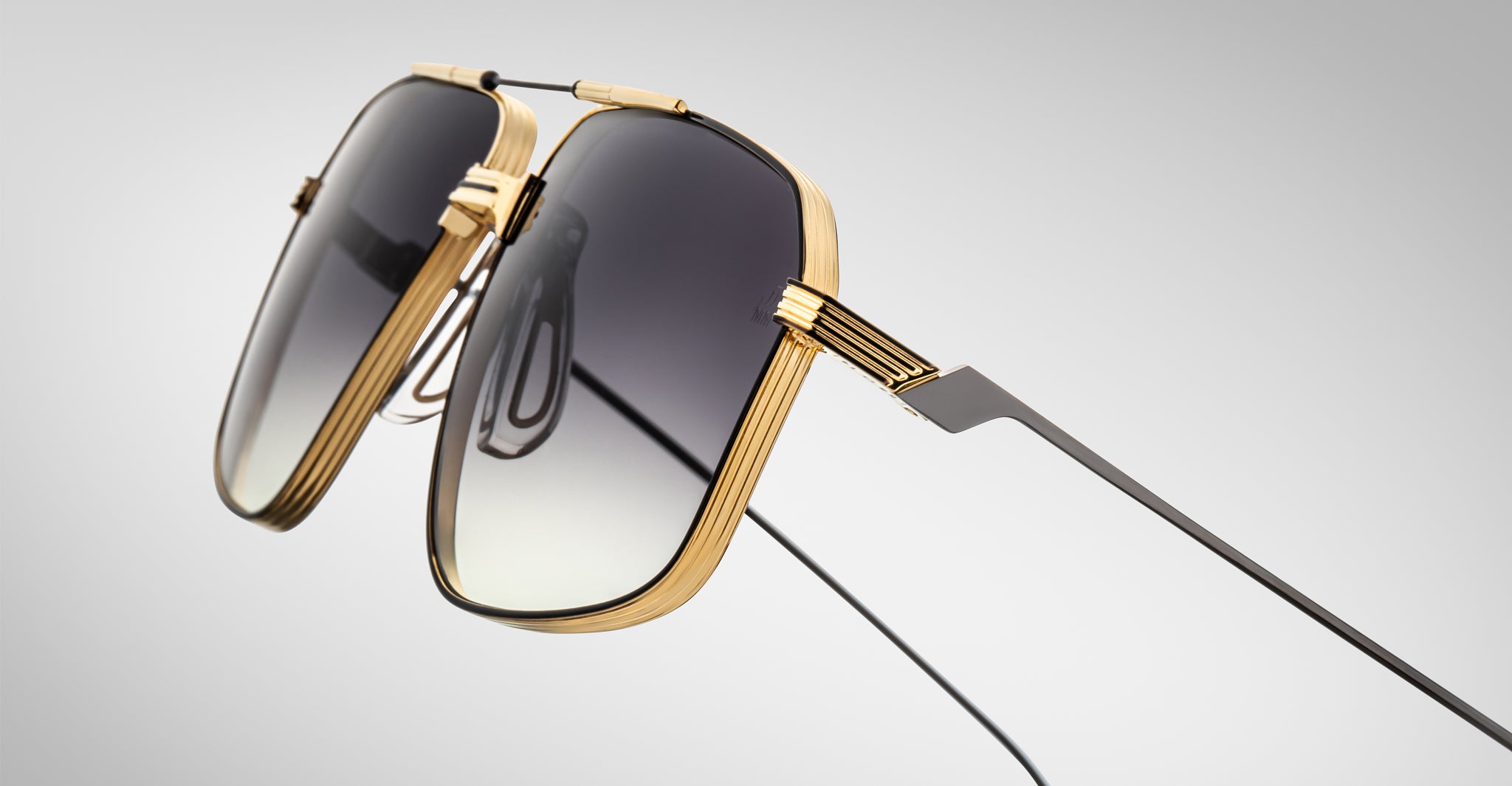 Close-up of Jacques Marie Mage Jagger oversized aviator sunglasses by Jacques Marie Mage, featuring gold beta titanium frames and dark gradient lenses, set against a plain light gray background.