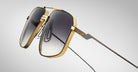 Close-up of Jacques Marie Mage Jagger oversized aviator sunglasses by Jacques Marie Mage, featuring gold beta titanium frames and dark gradient lenses, set against a plain light gray background.
