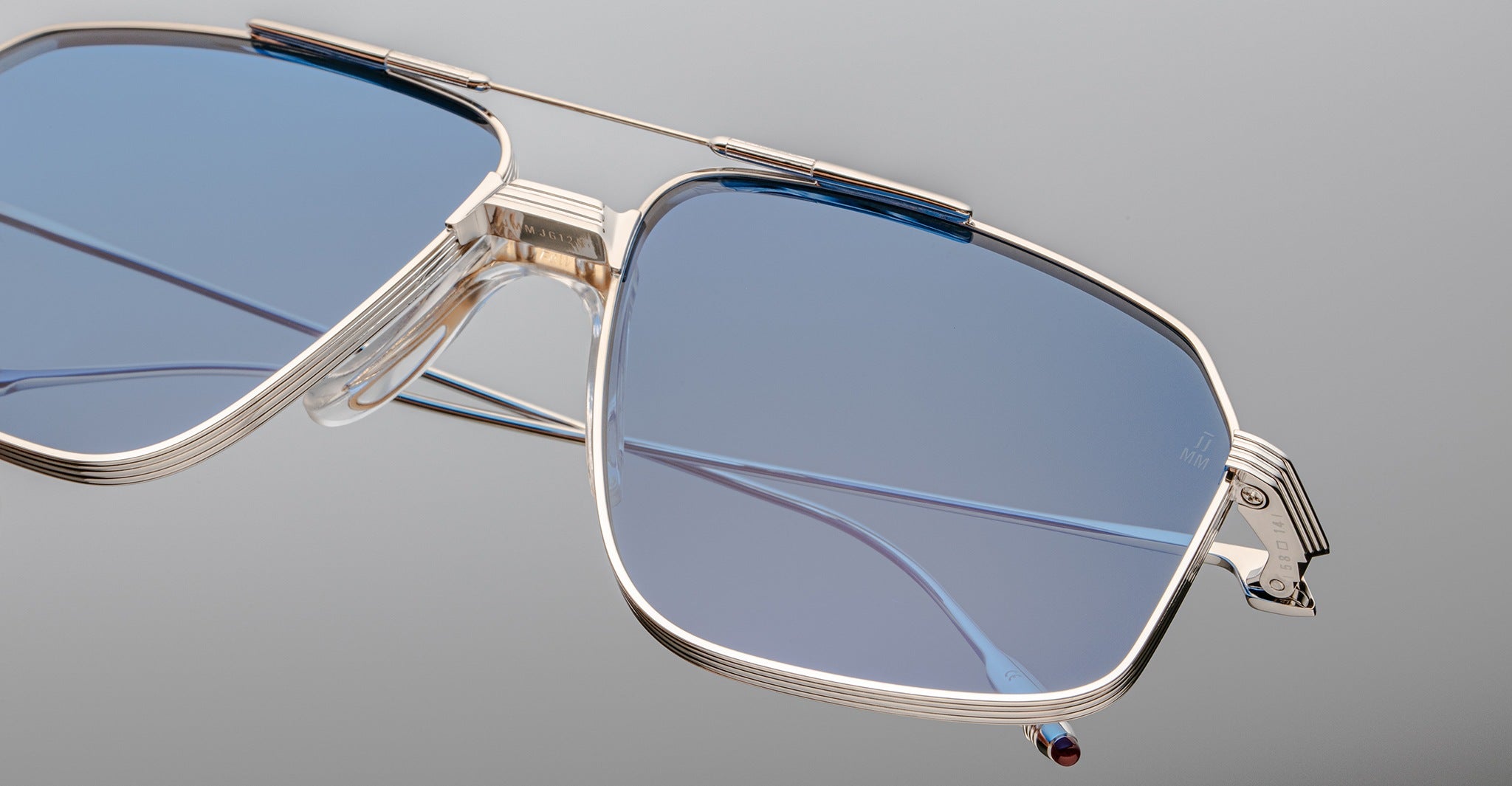 Close-up of the Jacques Marie Mage Jagger sunglasses by Jacques Marie Mage, featuring oversized aviator frames in silver beta titanium and blue-tinted lenses, highlighting their intricate design against a neutral background.