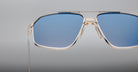 Close-up of Jacques Marie Mage Jagger sunglasses by Jacques Marie Mage, featuring oversized aviator design, blue tinted lenses, and thin beta titanium frames set against a plain grey background.