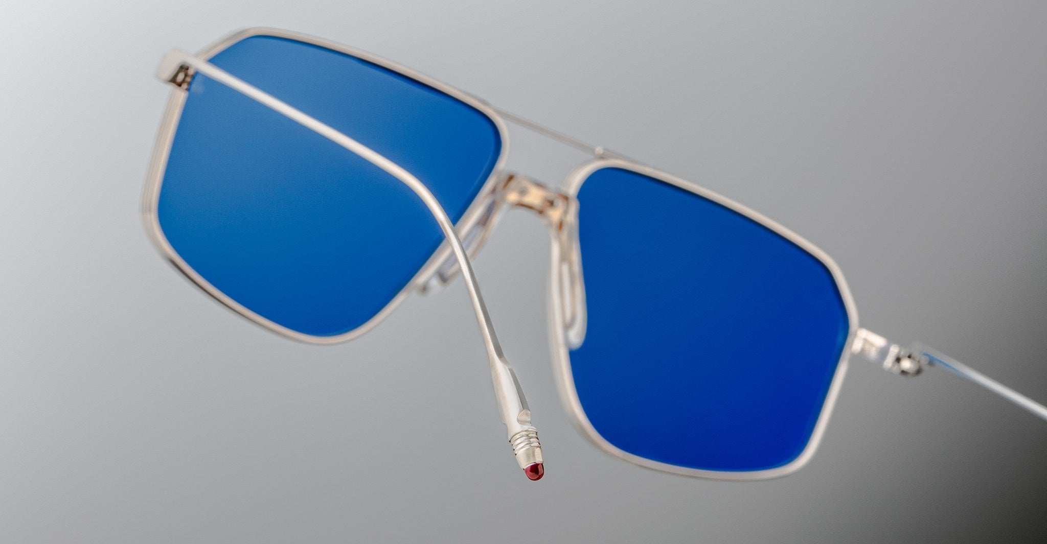 The Jacques Marie Mage Jagger sunglasses by Jacques Marie Mage feature silver oversized aviator frames with striking blue lenses, shown close-up against a neutral background.