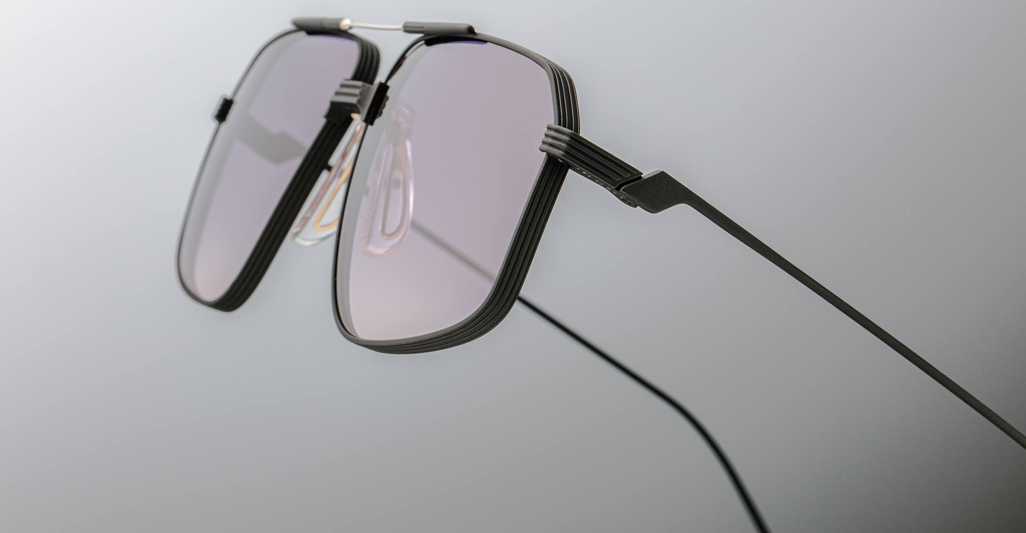 Close-up of Jacques Marie Mage Jagger eyeglasses by Jacques Marie Mage, featuring thin black beta titanium frames and lightly tinted lenses set against a plain, light grey background.