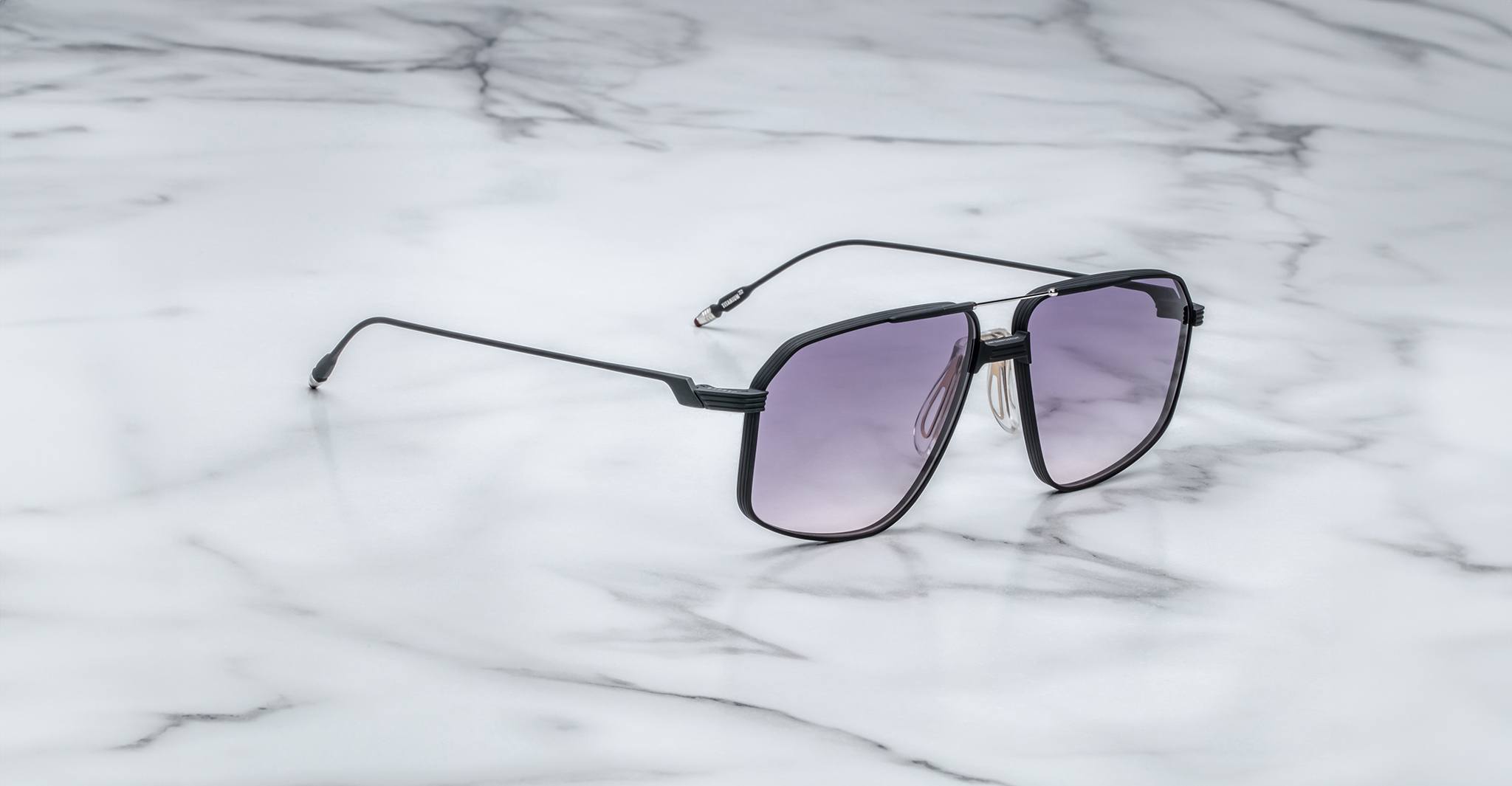 The Jacques Marie Mage Jagger, a pair of oversized aviator sunglasses by Jacques Marie Mage with black frames and gradient lenses, rests on a white marble surface.