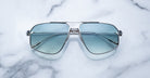 Jacques Marie Mage Jagger sunglasses by Jacques Marie Mage, featuring blue-tinted oversized aviator lenses, are displayed elegantly on a white marble surface.