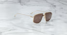 Jacques Marie Mage Jagger gold-framed oversized aviator sunglasses with brown lenses by Jacques Marie Mage rest elegantly on a white marble surface with grey veining.