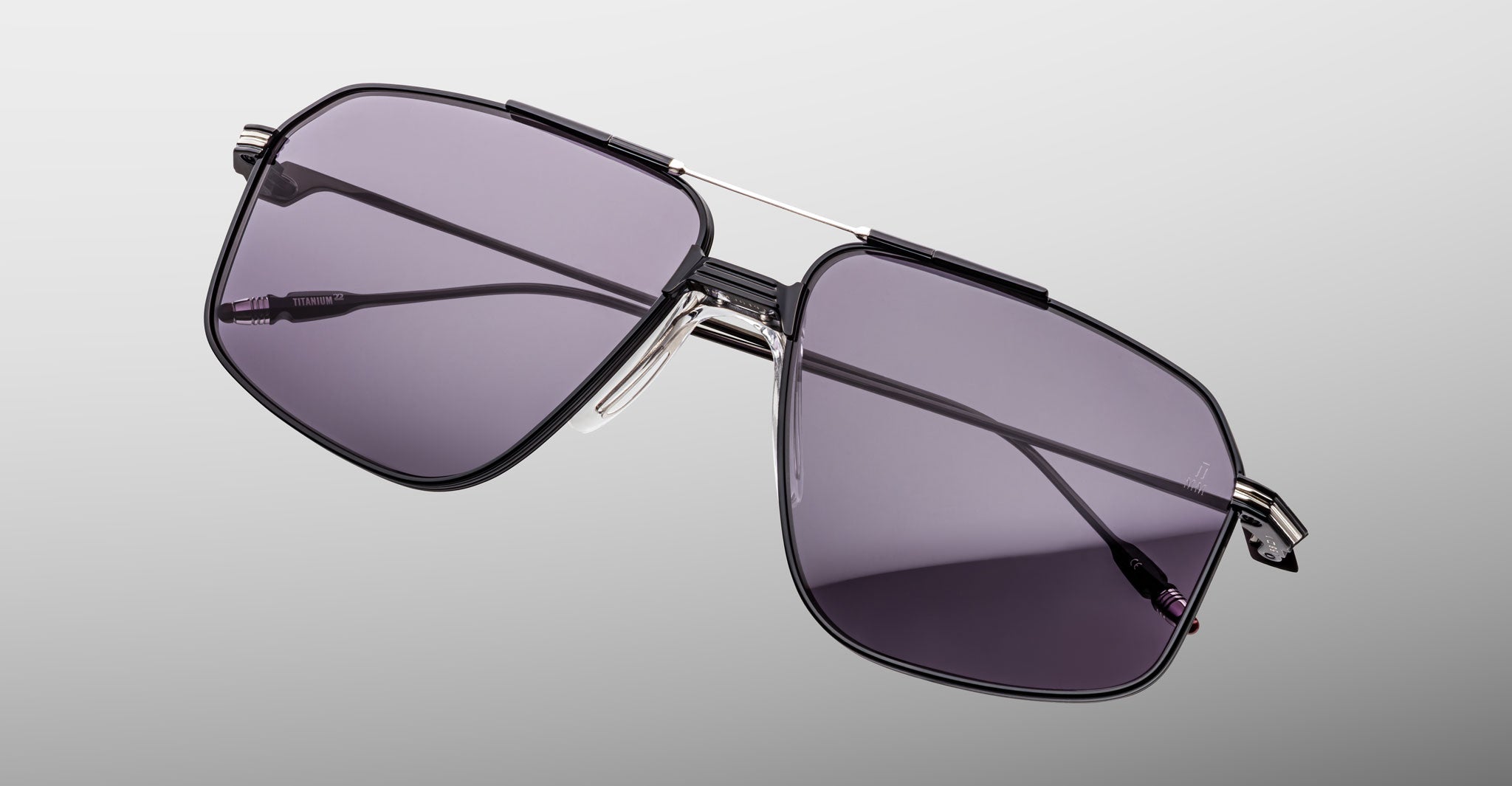 The Jacques Marie Mage Jagger aviator sunglasses, featuring a black Beta Titanium frame and dark gray tinted lenses, are displayed against a light gray background.