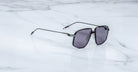 A pair of Jacques Marie Mage Jagger sunglasses by Jacques Marie Mage, featuring an oversized aviator shape with dark lenses and beta titanium accents, rests on a white marble surface.