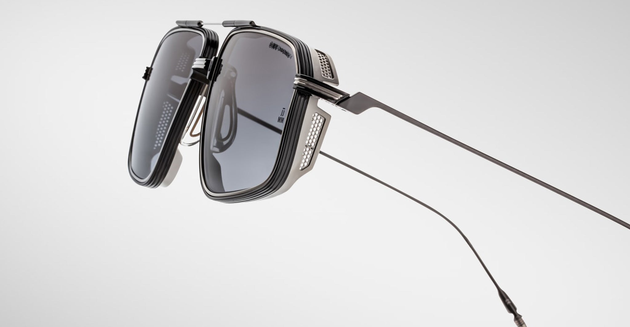 Close-up of Jacques Marie Mage Jagger sunglasses: futuristic, angular design with dark lenses, metal side shields, and thin beta titanium temples by Jacques Marie Mage, shown against a plain light background.