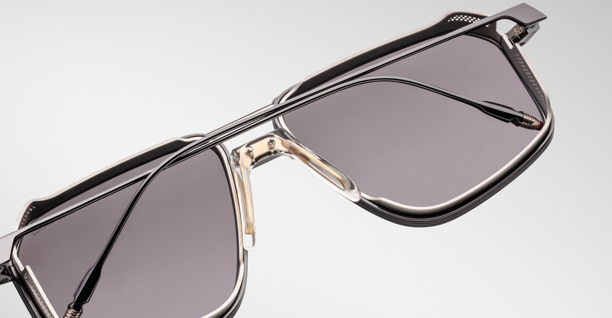 Close-up of Jacques Marie Mage Jagger sunglasses by Jacques Marie Mage, showcasing oversized aviator frames with dark tinted lenses, a double bridge, and sleek beta titanium accents set against a light background.