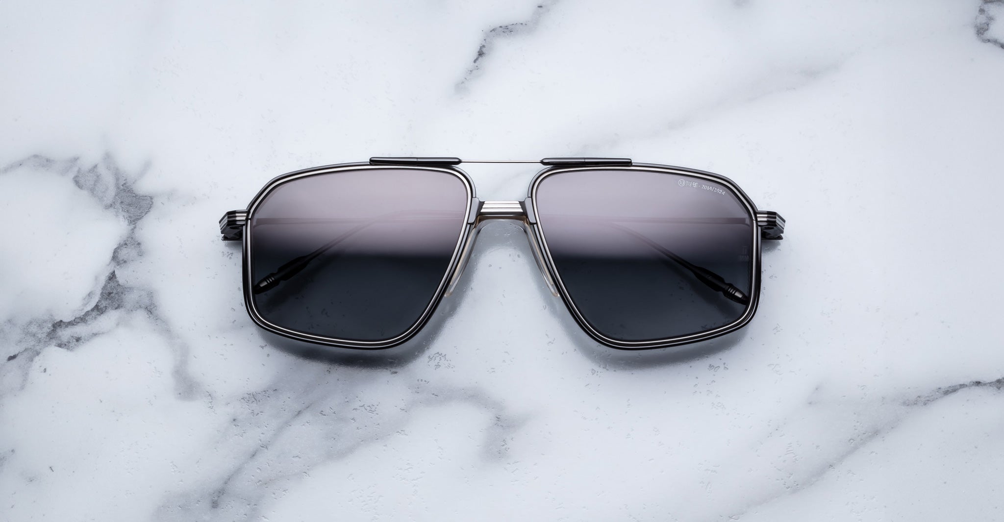 The Jacques Marie Mage Jagger sunglasses by Jacques Marie Mage, featuring black square beta titanium metal frames, rest on a white marble surface.