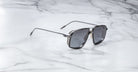 The Jacques Marie Mage Jagger by Jacques Marie Mage are modern black oversized aviator sunglasses with metallic temple detailing, crafted from beta titanium, displayed on a white marble surface.