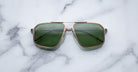 A pair of Jacques Marie Mage Jagger oversized aviator sunglasses with green lenses and gold beta titanium frames by Jacques Marie Mage sits on a white marble surface.