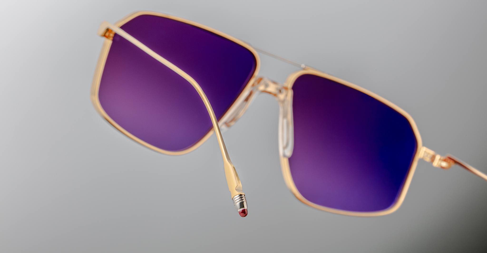 Jacques Marie Mage Jagger sunglasses feature gold beta titanium oversized aviator frames with square purple-tinted lenses and a quirky pencil eraser tip on the left arm, embodying the brand’s distinctive flair.