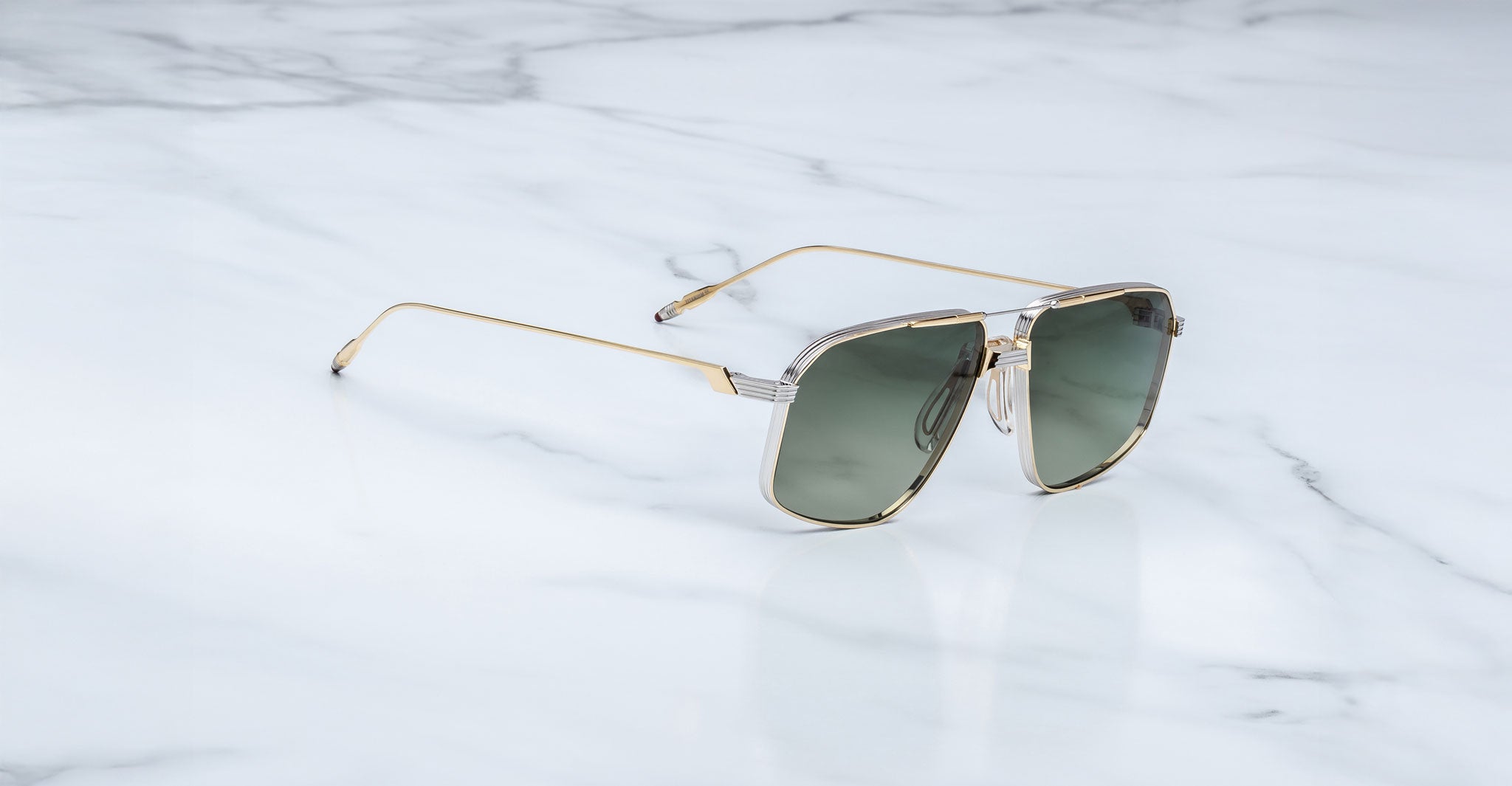 The Jacques Marie Mage Jagger sunglasses by Jacques Marie Mage feature oversized gold aviator frames and dark lenses, elegantly displayed on a white marble surface.