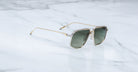 The Jacques Marie Mage Jagger sunglasses by Jacques Marie Mage feature oversized gold aviator frames and dark lenses, elegantly displayed on a white marble surface.