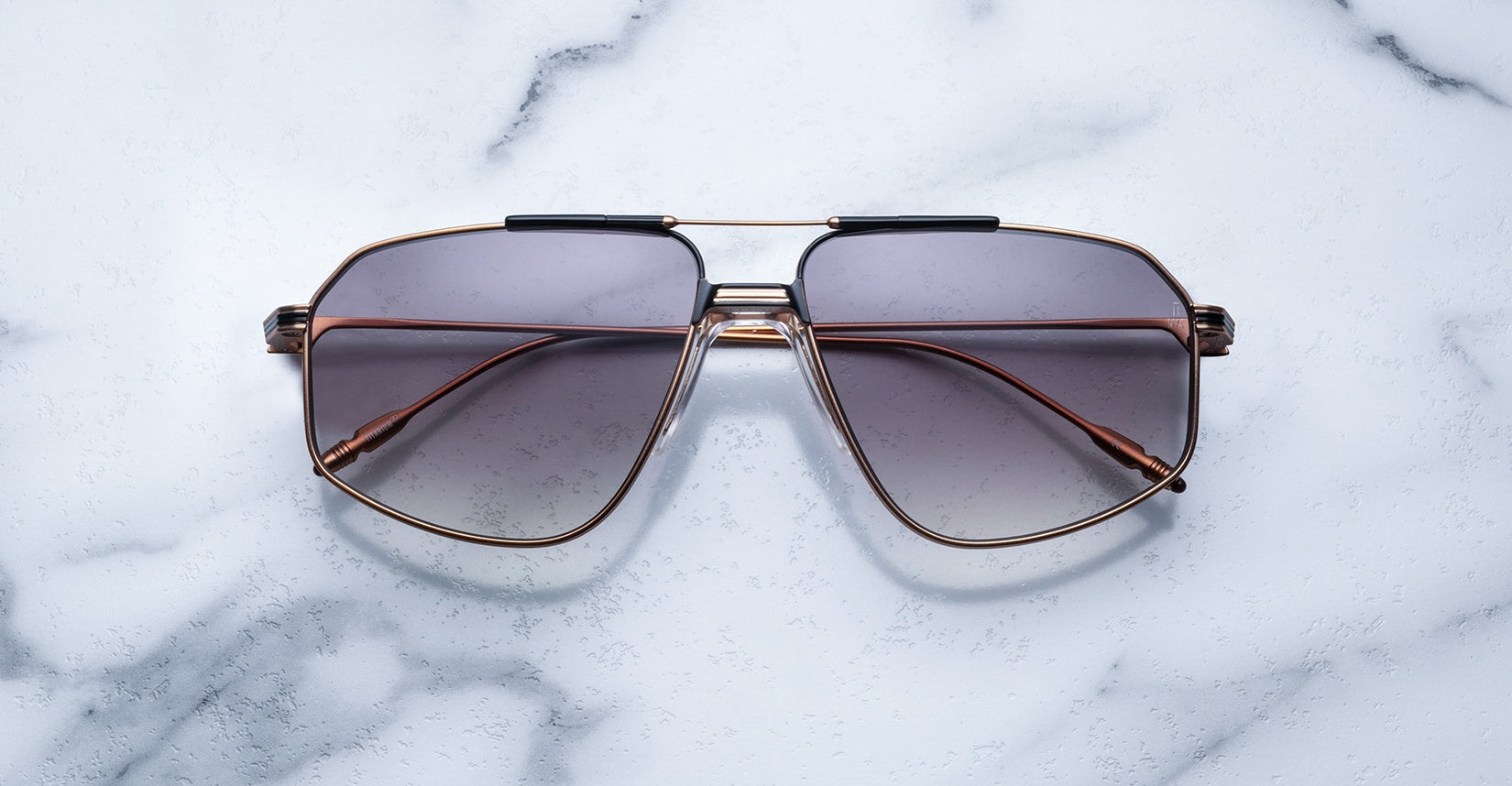 The Jacques Marie Mage Jagger sunglasses feature oversized aviator-style brown gradient lenses and slim beta titanium frames by Jacques Marie Mage, displayed on a white marble surface.