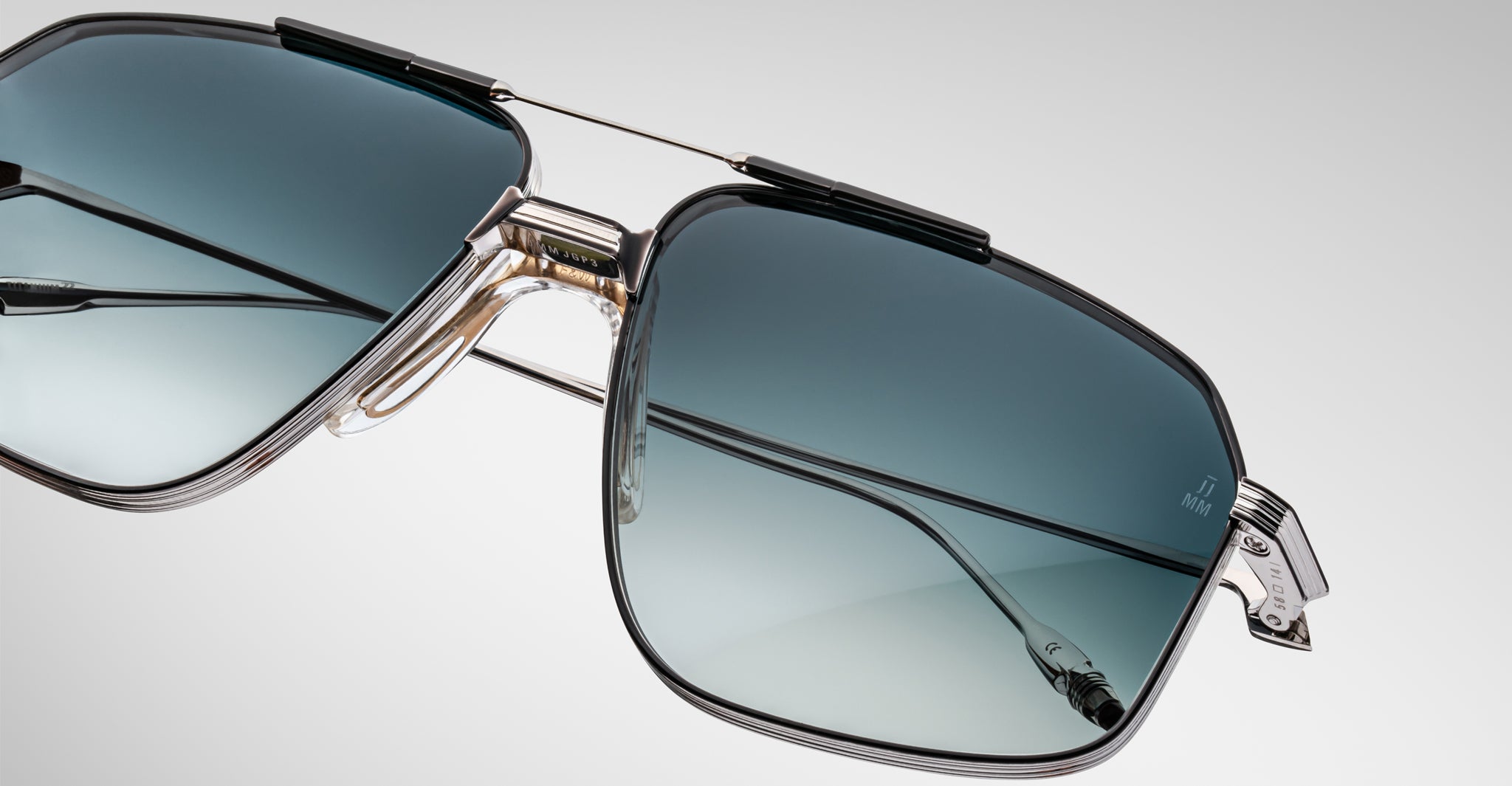 Close-up of Jacques Marie Mage Jagger sunglasses, featuring an oversized aviator design with blue gradient lenses, a silver beta titanium frame, and transparent nose pads against a plain light background.