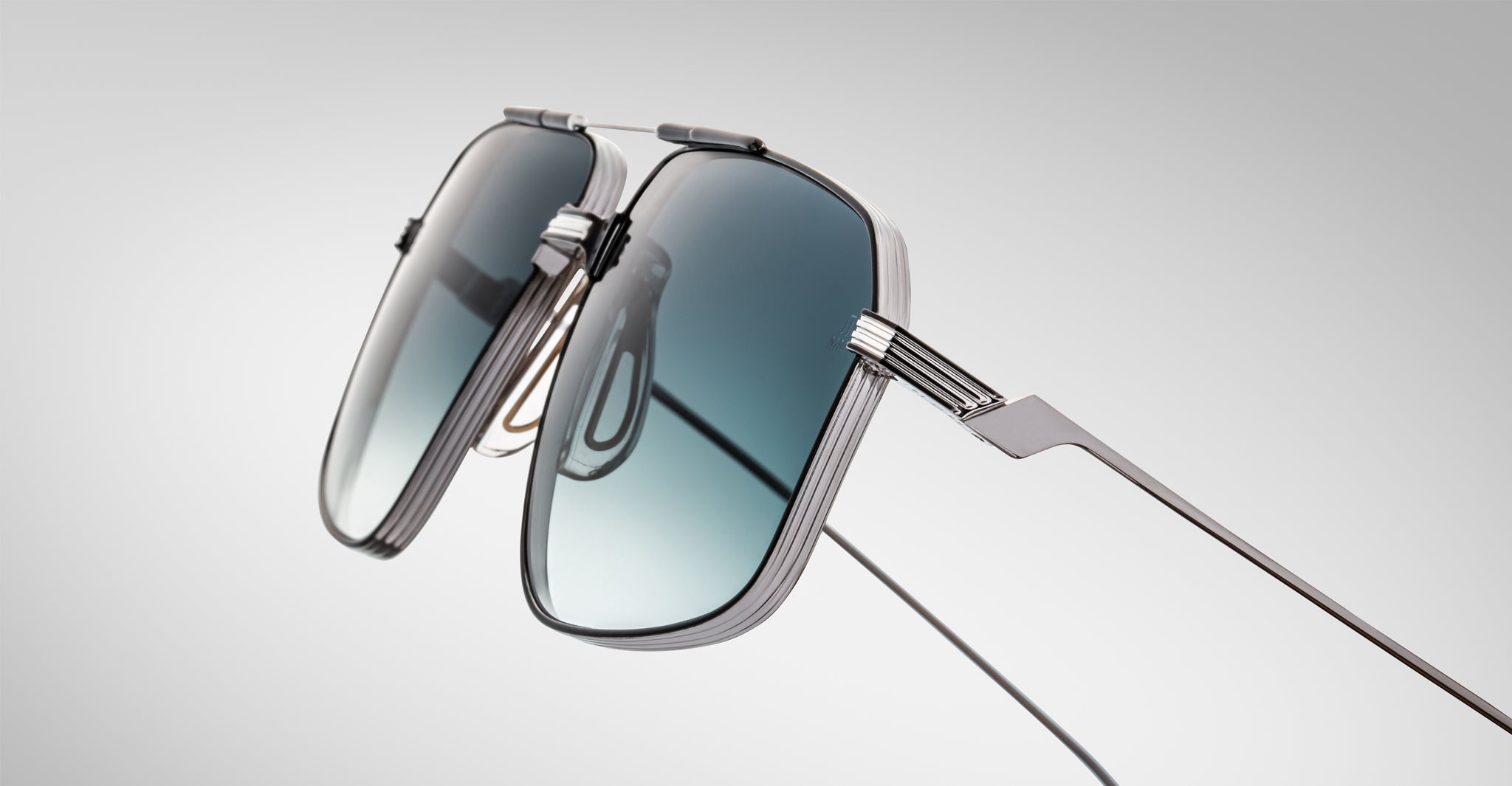 Close-up of Jacques Marie Mage Jagger sunglasses by Jacques Marie Mage, showcasing oversized aviator style with a sleek metallic frame and gradient blue lenses against a plain light gray background.