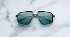 Jacques Marie Mage Jagger sunglasses feature teal lenses and a square frame, shown from above.