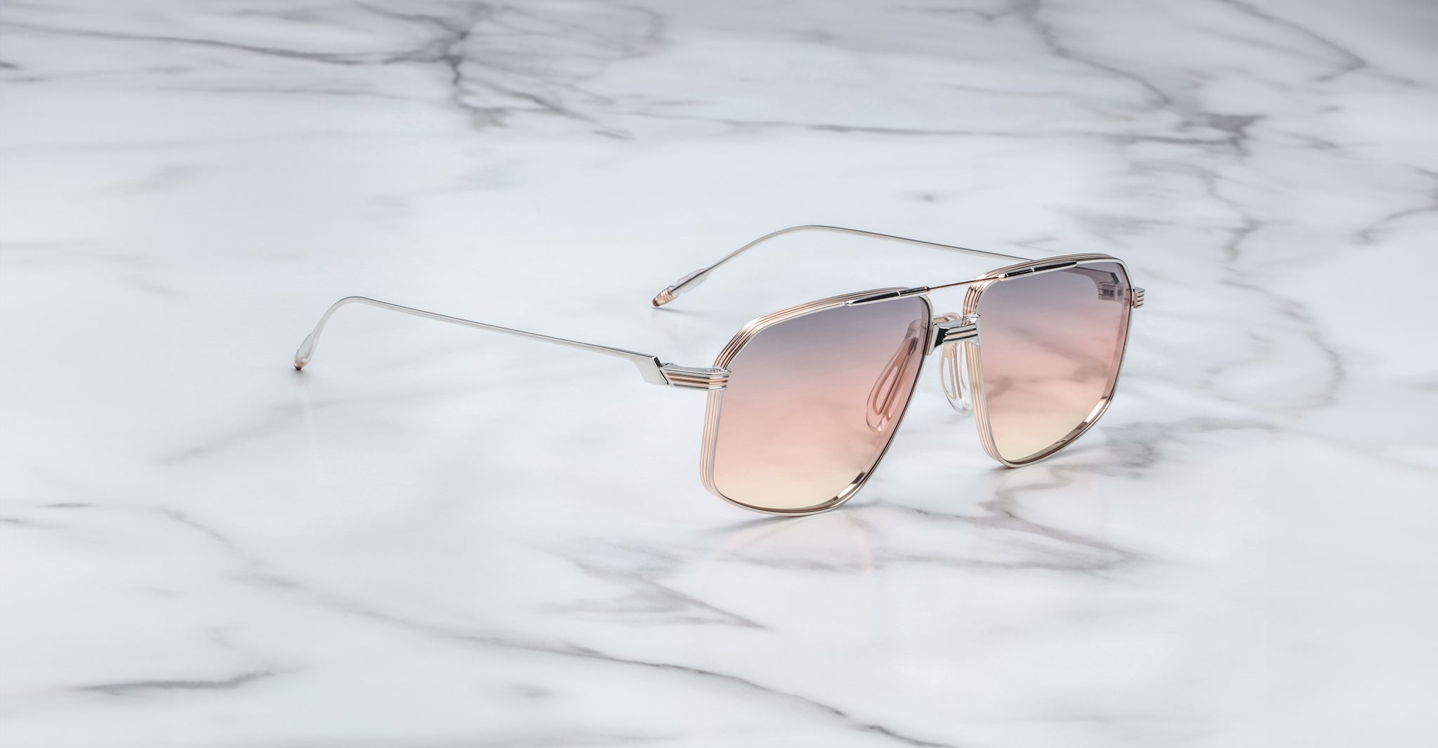 A pair of Jacques Marie Mage Jagger oversized aviator sunglasses with pink gradient lenses and thin beta titanium frames from Jacques Marie Mage, elegantly displayed on a white marble surface.