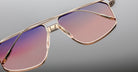 Close-up of Jacques Marie Mage Jagger oversized aviator sunglasses with gold frames and gradient pink to purple lenses, set against a light gray background.