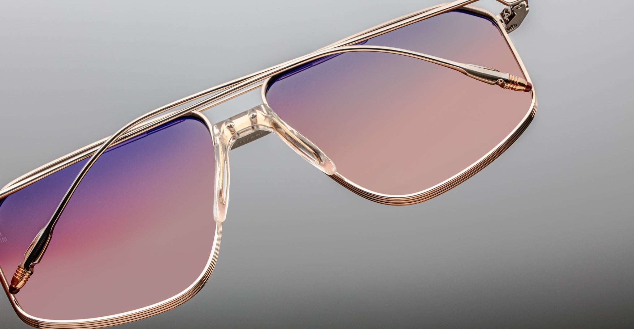 Close-up of Jacques Marie Mage Jagger oversized aviator sunglasses with gold frames and gradient pink to purple lenses, set against a light gray background.