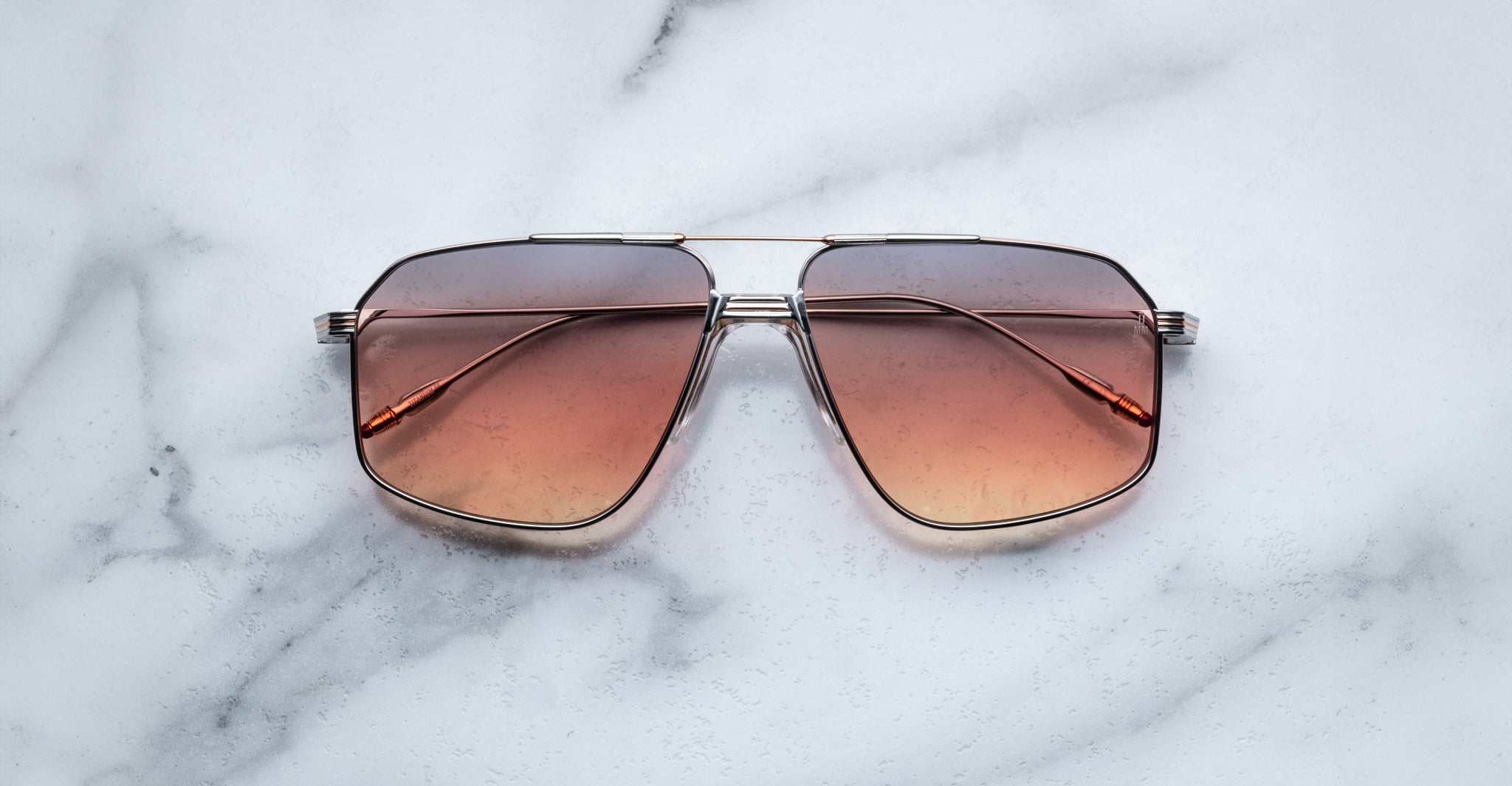 The Jacques Marie Mage Jagger sunglasses by Jacques Marie Mage, featuring oversized aviator gradient brown-tinted lenses and thin beta titanium frames, rest on a white marble surface.