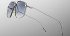 The Jacques Marie Mage Jagger sunglasses by Jacques Marie Mage feature silver oversized aviator frames with blue-tinted lenses, shown against a gray gradient background and angled to showcase thin beta titanium arms.