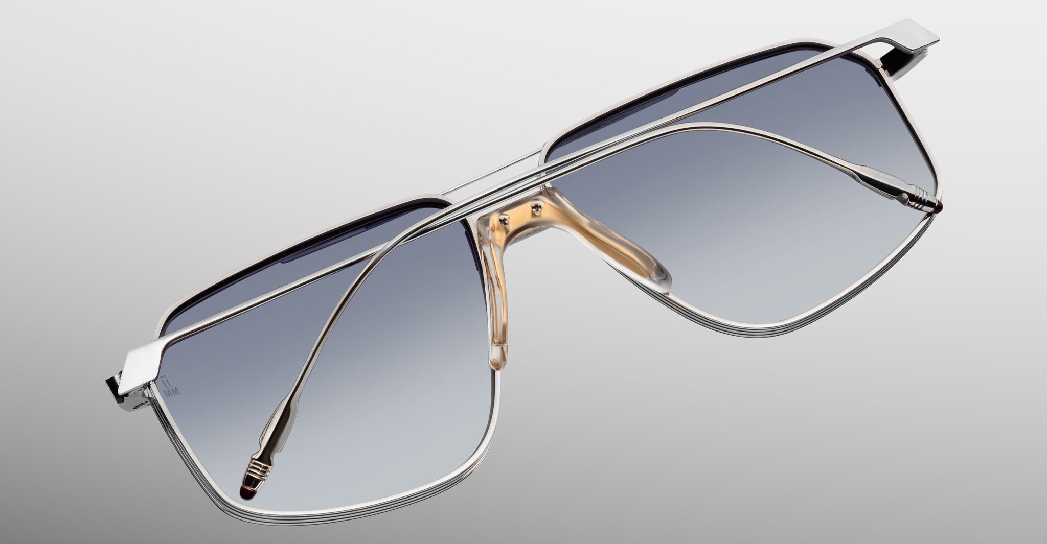 Jacques Marie Mage Jagger: Oversized aviator sunglasses in silver beta titanium with gradient blue lenses and gold nose pads by Jacques Marie Mage, shown on a light gray background for a bold, timeless style.