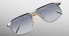 Jacques Marie Mage Jagger: Oversized aviator sunglasses in silver beta titanium with gradient blue lenses and gold nose pads by Jacques Marie Mage, shown on a light gray background for a bold, timeless style.