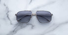 A pair of Jacques Marie Mage Jagger oversized aviator sunglasses with dark lenses and sleek metal frames from Jacques Marie Mage rests on a light marble surface.