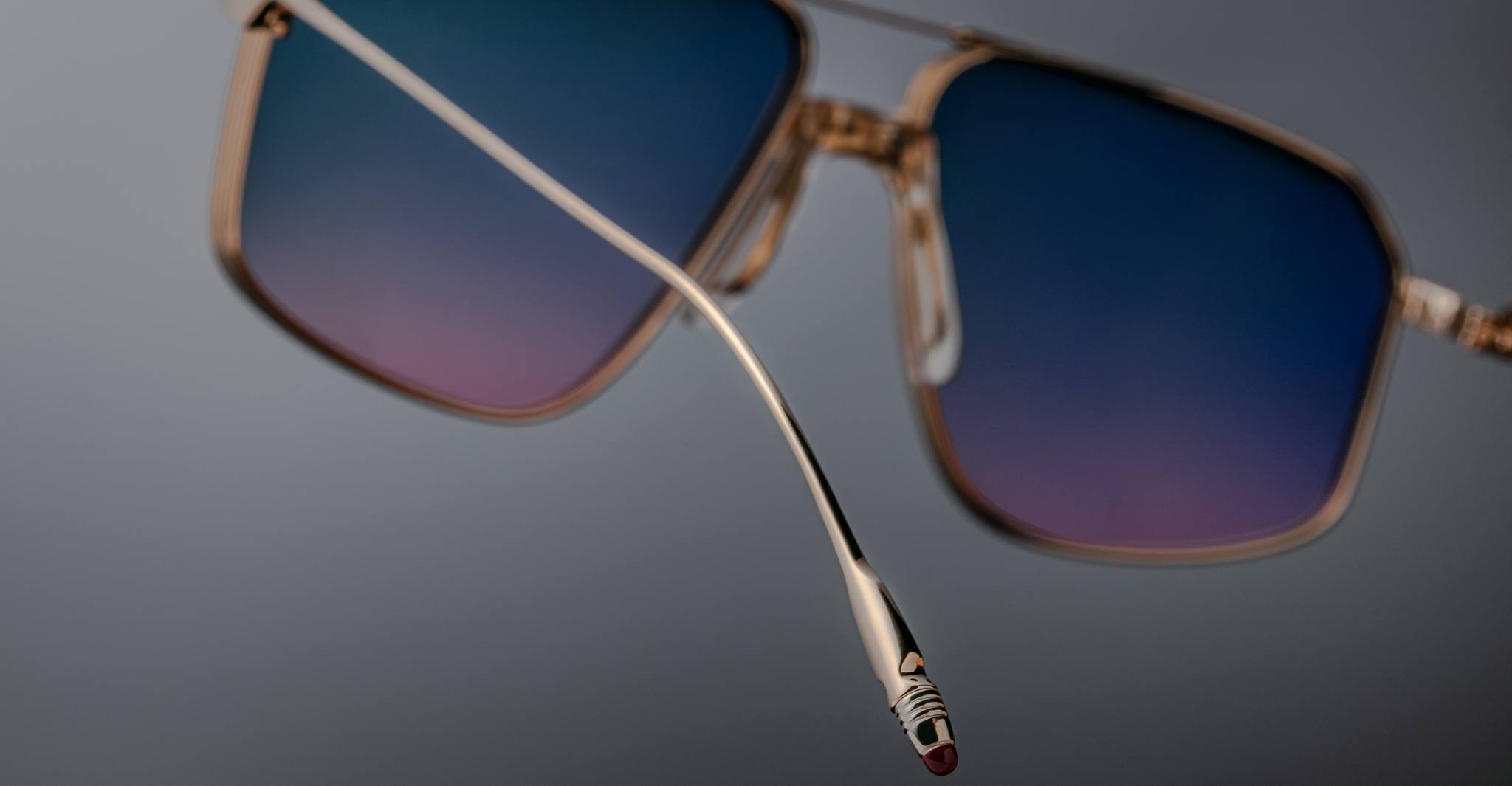 Close-up of Jacques Marie Mage Jagger oversized aviator sunglasses by Jacques Marie Mage, featuring gold-rimmed frames, blue gradient lenses, and a focus on the temple arm's beta titanium build with detailed tip design.