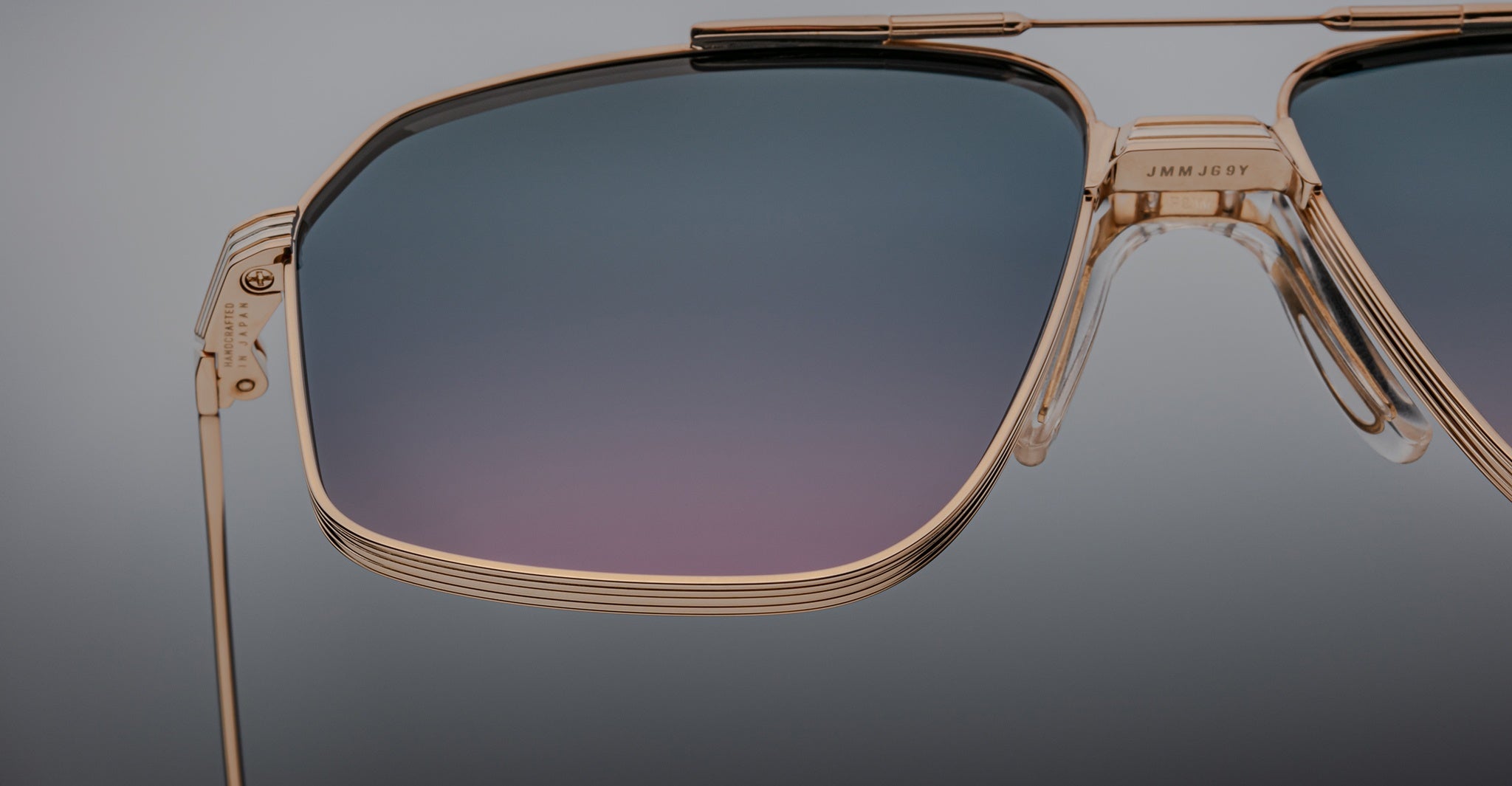 Close-up of Jacques Marie Mage Jagger sunglasses by Jacques Marie Mage, featuring oversized aviator gold frames and gradient blue-purple lenses, set against a plain background.