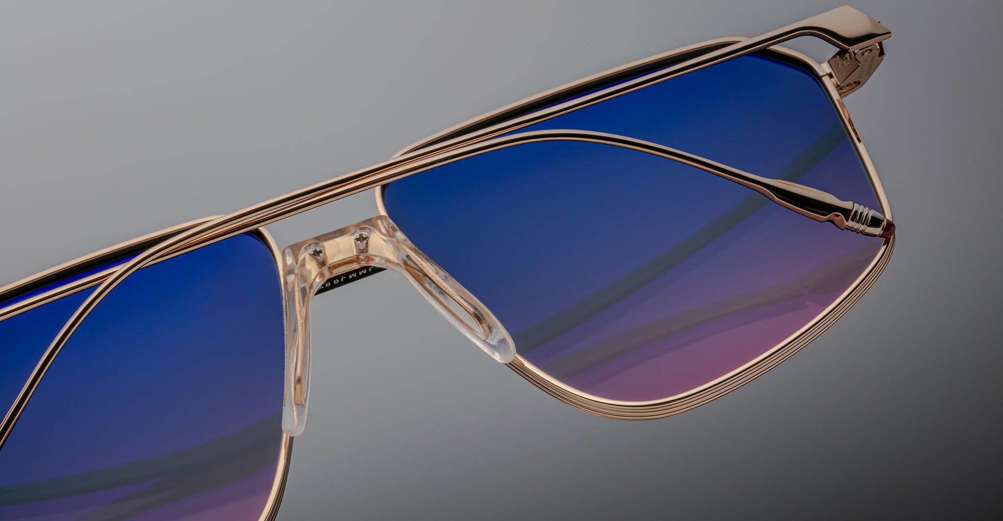 Close-up of Jacques Marie Mage Jagger oversized aviator sunglasses by Jacques Marie Mage, featuring gold metal frames and blue-to-purple gradient lenses, set against a neutral background.